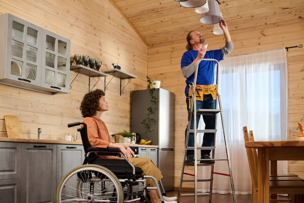 Young woman with disability looking at electrician changing bulbs in chandelier